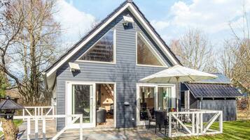 A modern two-story house with a sloped roof, large windows, and a covered patio area.