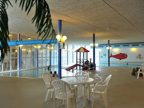 An indoor swimming pool with a slide, seating area, and decorative fish murals.