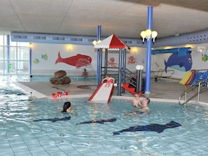 An indoor swimming pool with a slide, decorative fish murals, and a dolphin mural.