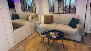 Un salon moderne avec un canapé beige, une table basse en verre et un grand miroir qui reflète la pièce.