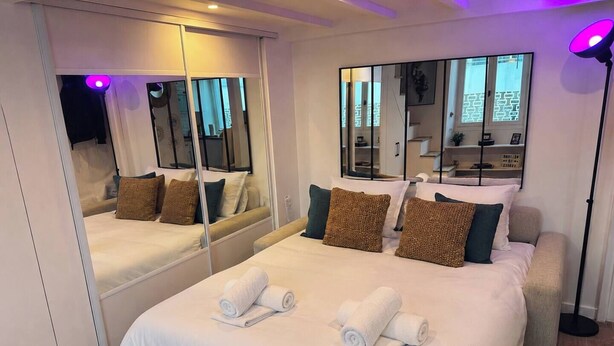 Une chambre d’hôtel avec un grand lit, deux miroirs de chevet, une lampe de chevet et un petit coin salon.