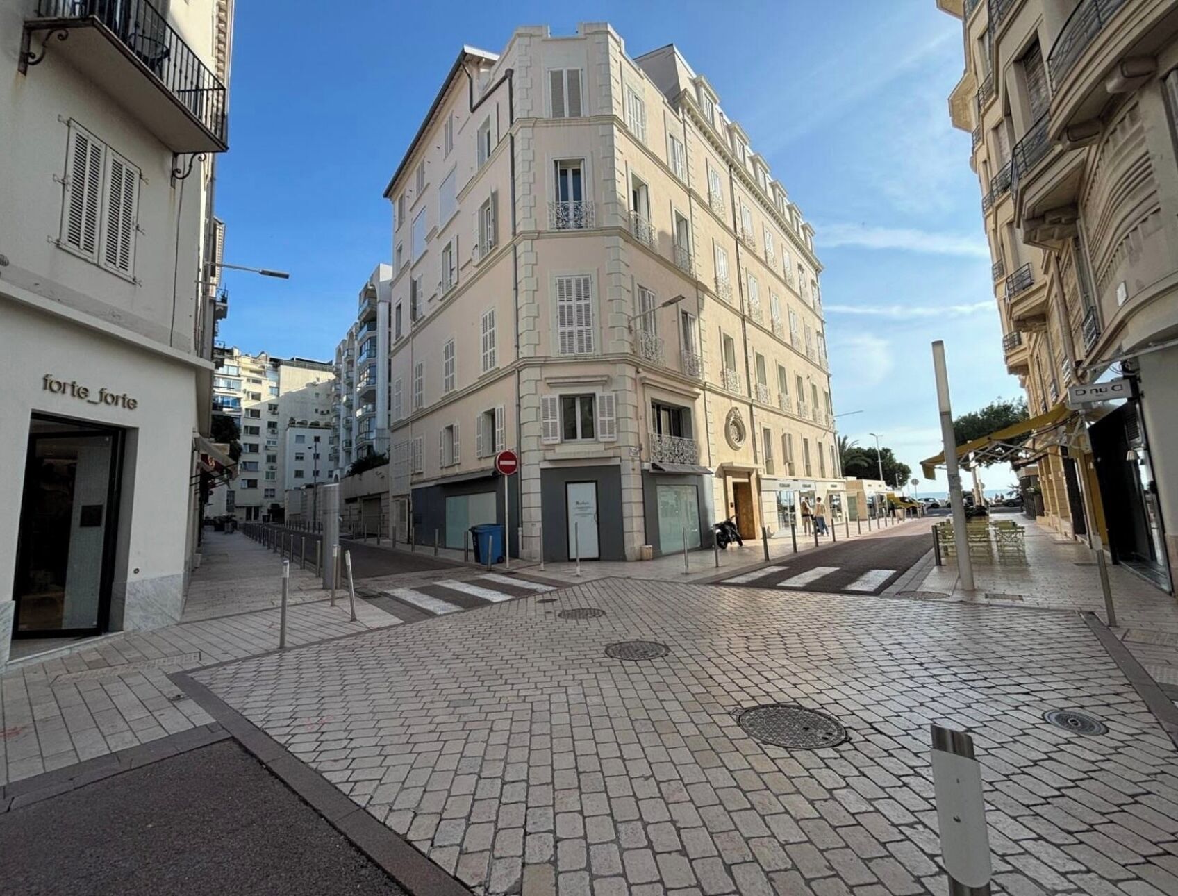 A street view with a building featuring a corner entrance, a visible door, and a sign above the entrance.