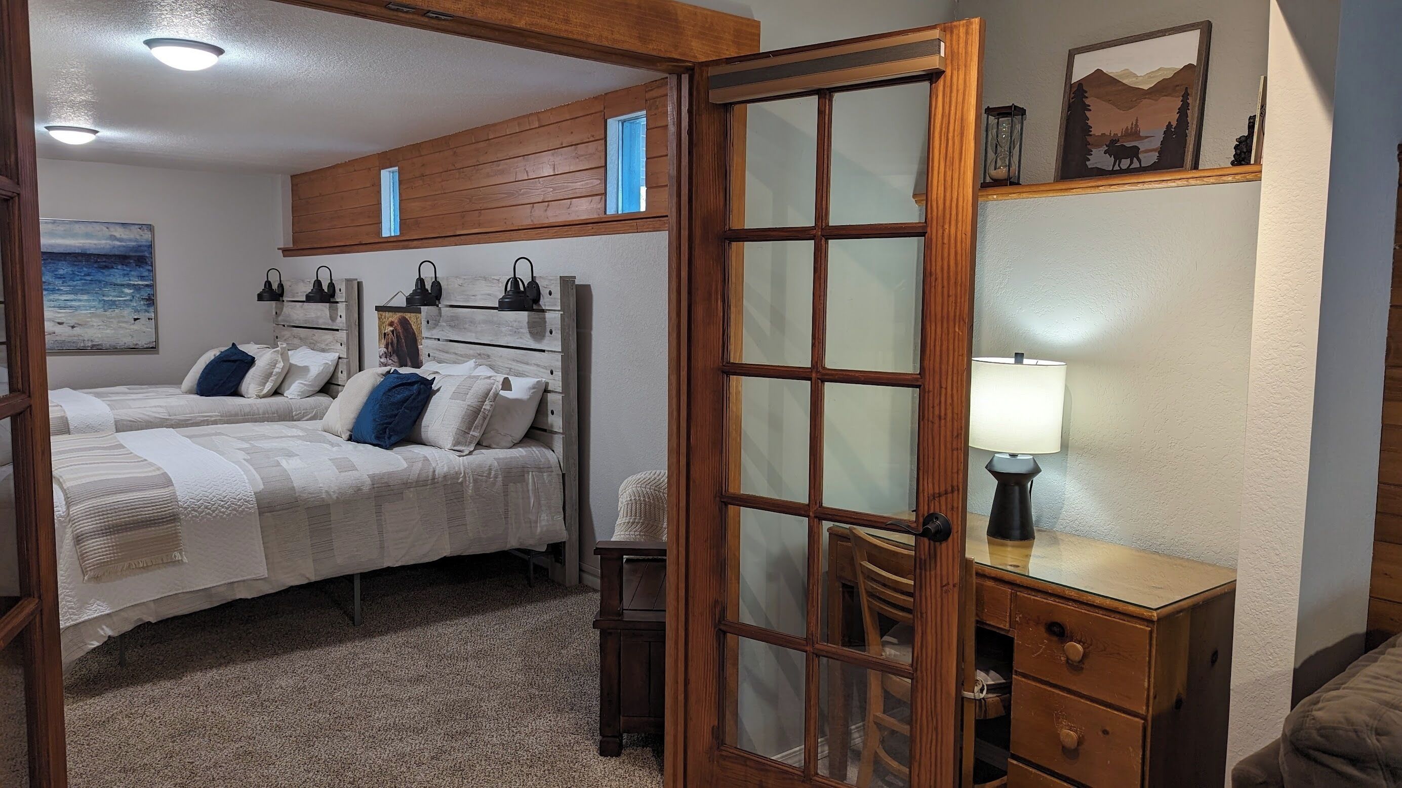 A bedroom with two beds, a wooden headboard, a nightstand, a lamp, and a painting on the wall.
