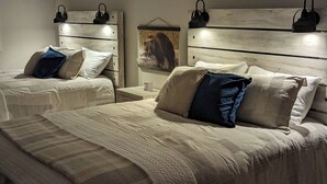 Un dormitorio con dos camas, cada una con cabecera y lámparas de noche. Hay un cuadro enmarcado en la pared entre las camas.