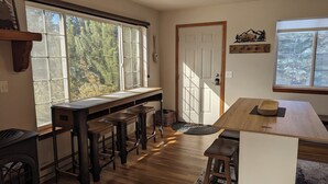 Una cocina con una mesa de madera larga, taburetes de bar y una estufa.