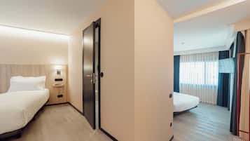 A hotel room with two beds, a nightstand, a lamp, and a view of the hallway.