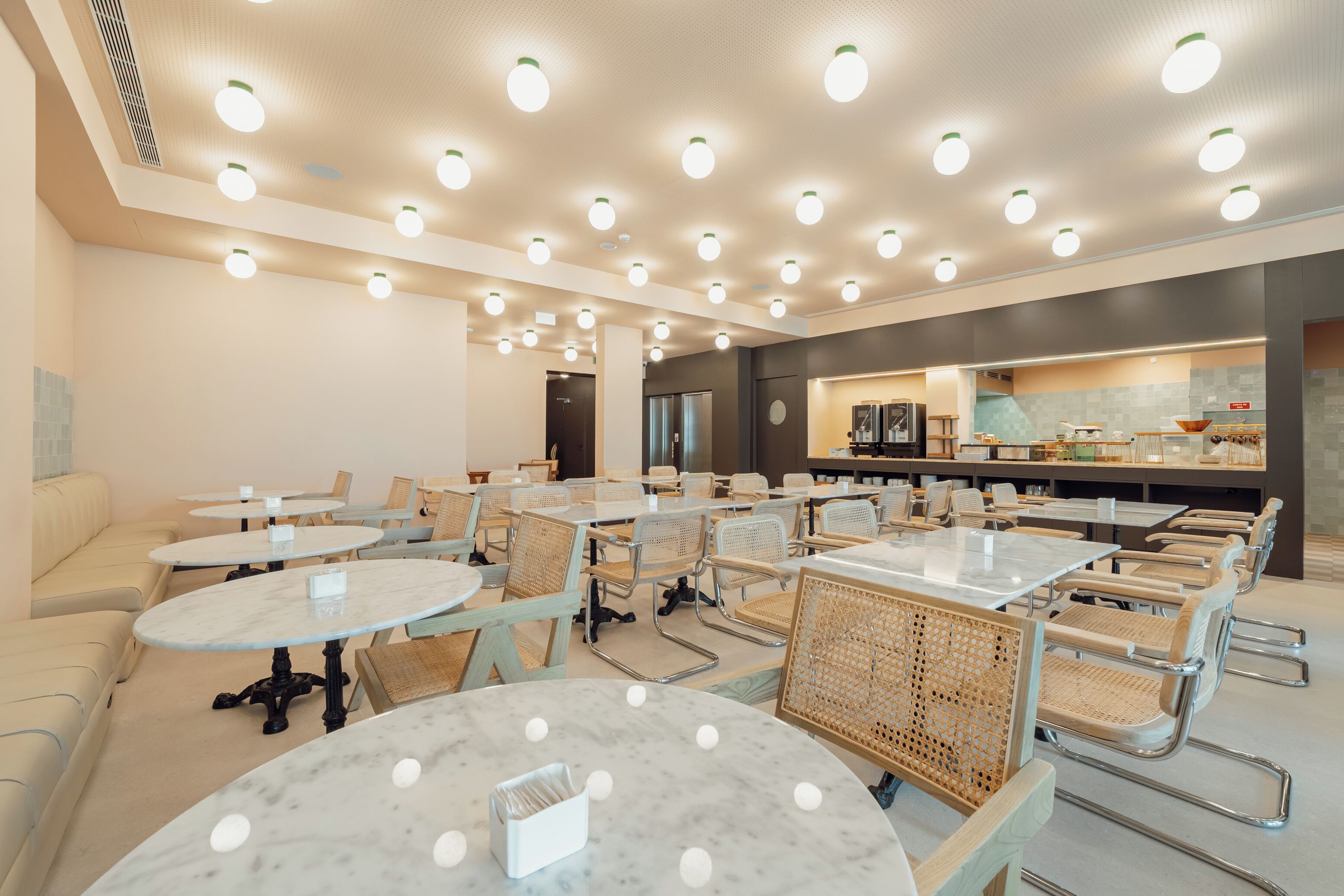 A modern cafe with round tables and wicker chairs, a counter with a menu, and a cozy seating area with a sofa.