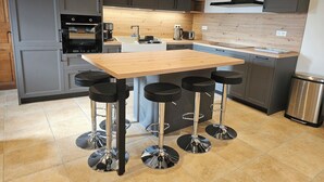 A modern kitchen with grey cabinets, a wooden island with bar stools, and stainless steel appliances. - Authentic Aubrac farmhouse with Jacuzzi. A change of scenery guaranteed! (Montpeyroux)