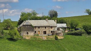 A stone house with a sloped roof, surrounded by a grassy field and trees. - Authentic Aubrac farmhouse with Jacuzzi. A change of scenery guaranteed! (Montpeyroux)