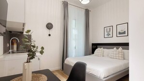Una habitación de hotel moderna con una cama, un escritorio con una silla, una planta, un reloj y dos cuadros en la pared.