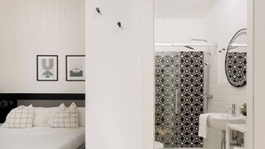 Un dormitorio moderno con cama, mesitas de noche y un pequeño tocador. Junto al dormitorio se encuentra un baño con ducha, lavabo e inodoro.