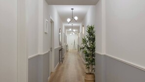 Un pasillo estrecho con paredes blancas, piso de madera y una planta en maceta a la derecha.