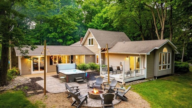 Ein zweistöckiges Haus mit überdachter Terrasse, Sitzgelegenheiten im Freien und einem Feuerkorb.