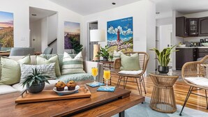 Ein modernes Wohnzimmer mit Couchtisch aus Holz, Korbstühlen und einem großen Poster mit einem Leuchtturm.