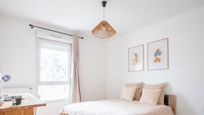 Ein Schlafzimmer mit einem Bett, einem Schreibtisch, einer Lampe, einem Fenster mit Vorhängen und zwei gerahmten Bildern an der Wand.