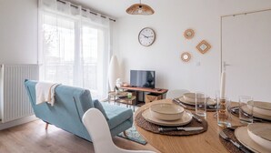 Ein modernes Wohnzimmer mit einer Couch, einem Esstisch für vier Personen, einem Fernseher und dekorativen Wandbildern.