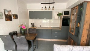 A modern kitchen with grey cabinets, a wooden dining table, and a grey sofa. - Vacation apartment Pingo 1 (Ahrbrück)