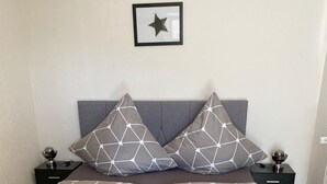 A neatly made bed with geometric-patterned bedding, two bedside tables with lamps, and a framed star decoration on the wall. - Vacation apartment Pingo 1 (Ahrbrück)