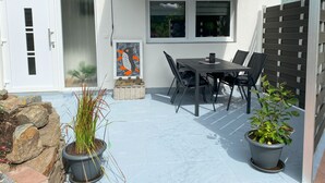 A patio with a table and chairs, a potted plant, and a wall-mounted artwork. - Vacation apartment Pingo 1 (Ahrbrück)