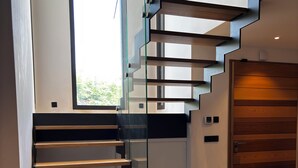 Un escalier moderne avec des rampes en verre et des marches en bois, menant à une pièce dotée d’une porte en bois et d’une petite fenêtre.