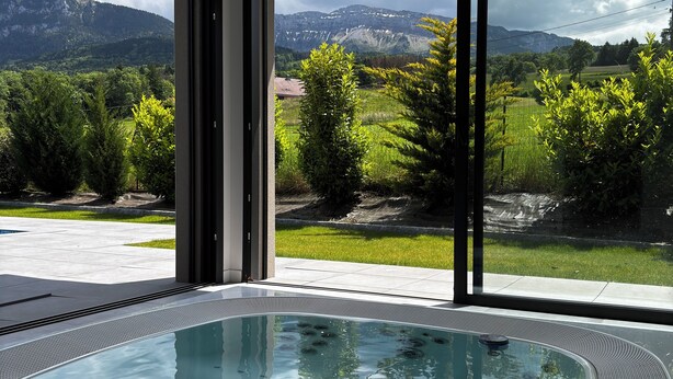 Un bain à remous intérieur moderne offrant une vue sur les montagnes et la verdure.