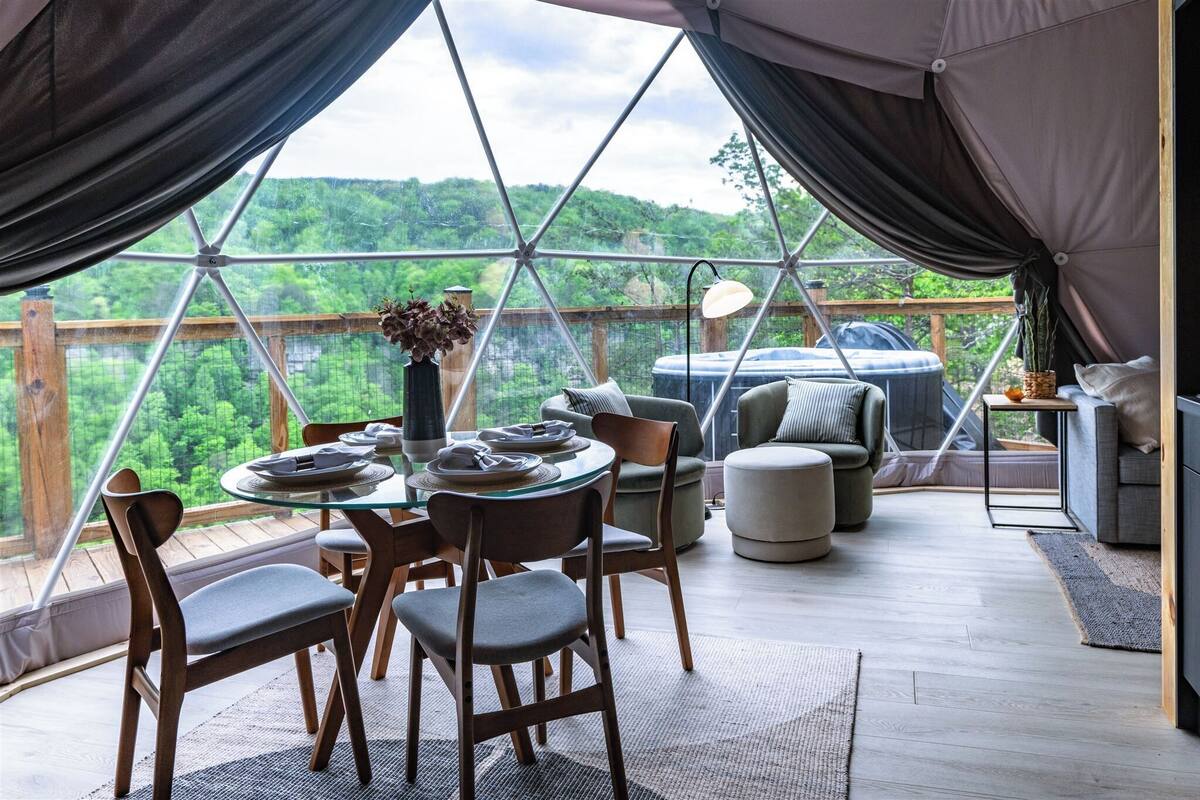 Ein gemütlicher Innenraum mit Esstisch, Stühlen und einer Couch, mit Blick auf einen üppigen grünen Wald.