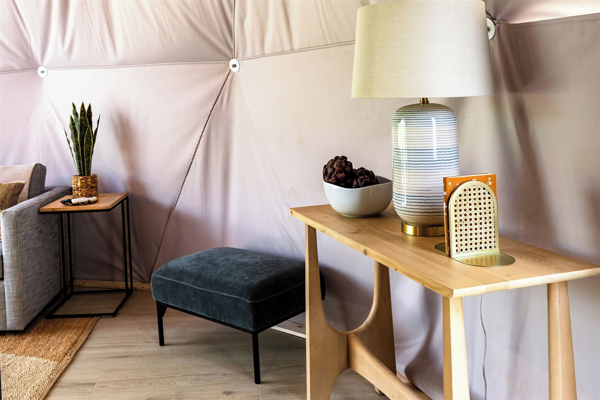 Une pièce accueillante avec un banc rembourré, une petite table avec une lampe, un bol rempli d'objets décoratifs et une plante en pot.