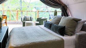 Een gezellige slaapkamer met een groot bed, een bank en een fauteuil, alles dichtbij een groot raam met uitzicht op het landschap.