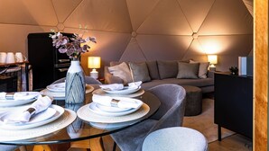 Een tentaccomodatie met een eettafel voor twee personen, een bank en een klein kastje.