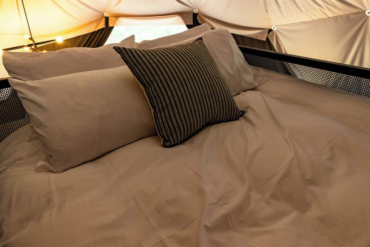 Ein Bett mit beigefarbener Bettwäsche und gestreifter Kissen in einer zeltartigen Konstruktion.