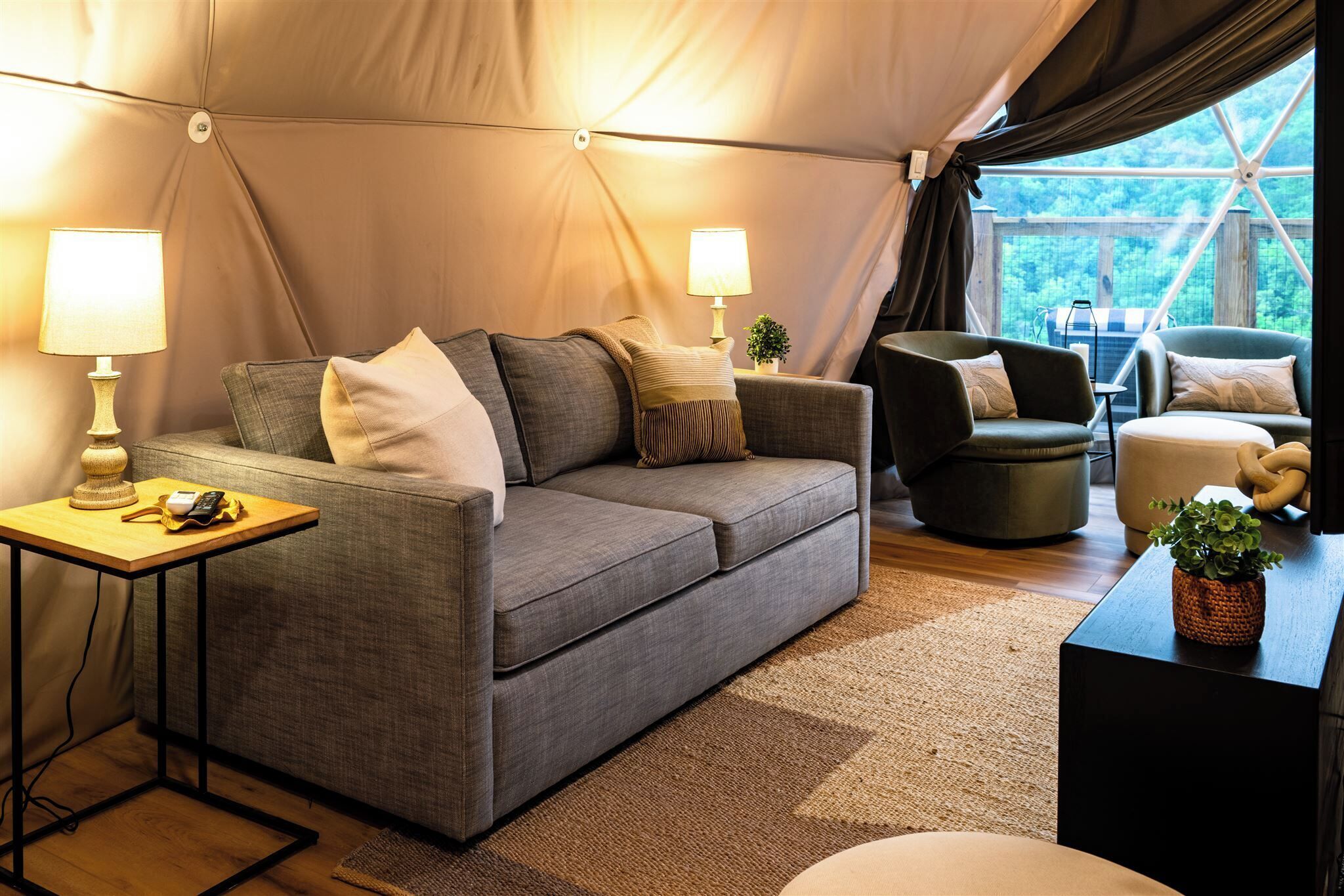 A cozy tented accommodation with a sofa, armchairs, and a small table with a lamp.