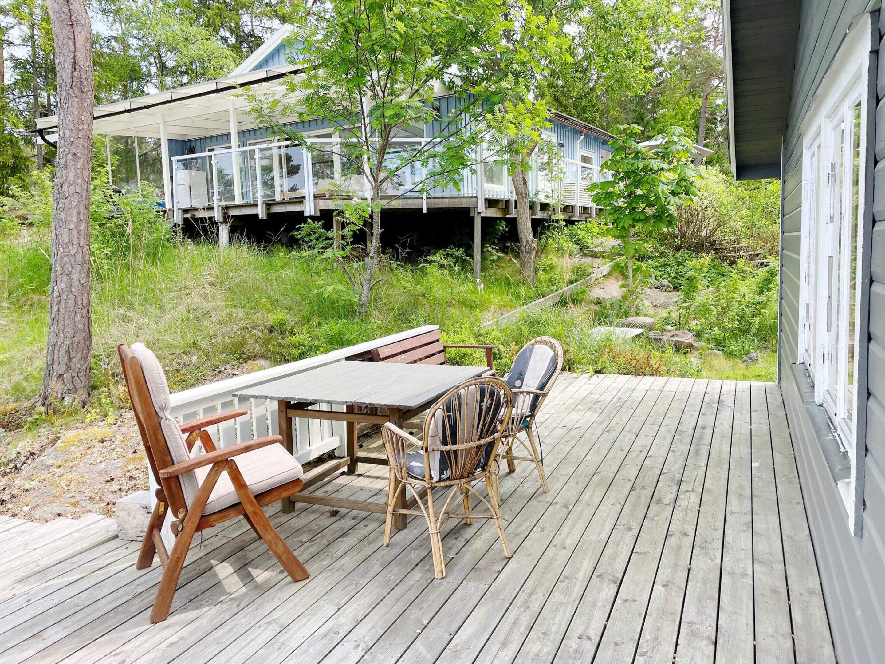 A wooden deck with a table and chairs, overlooking a house with a covered porch.