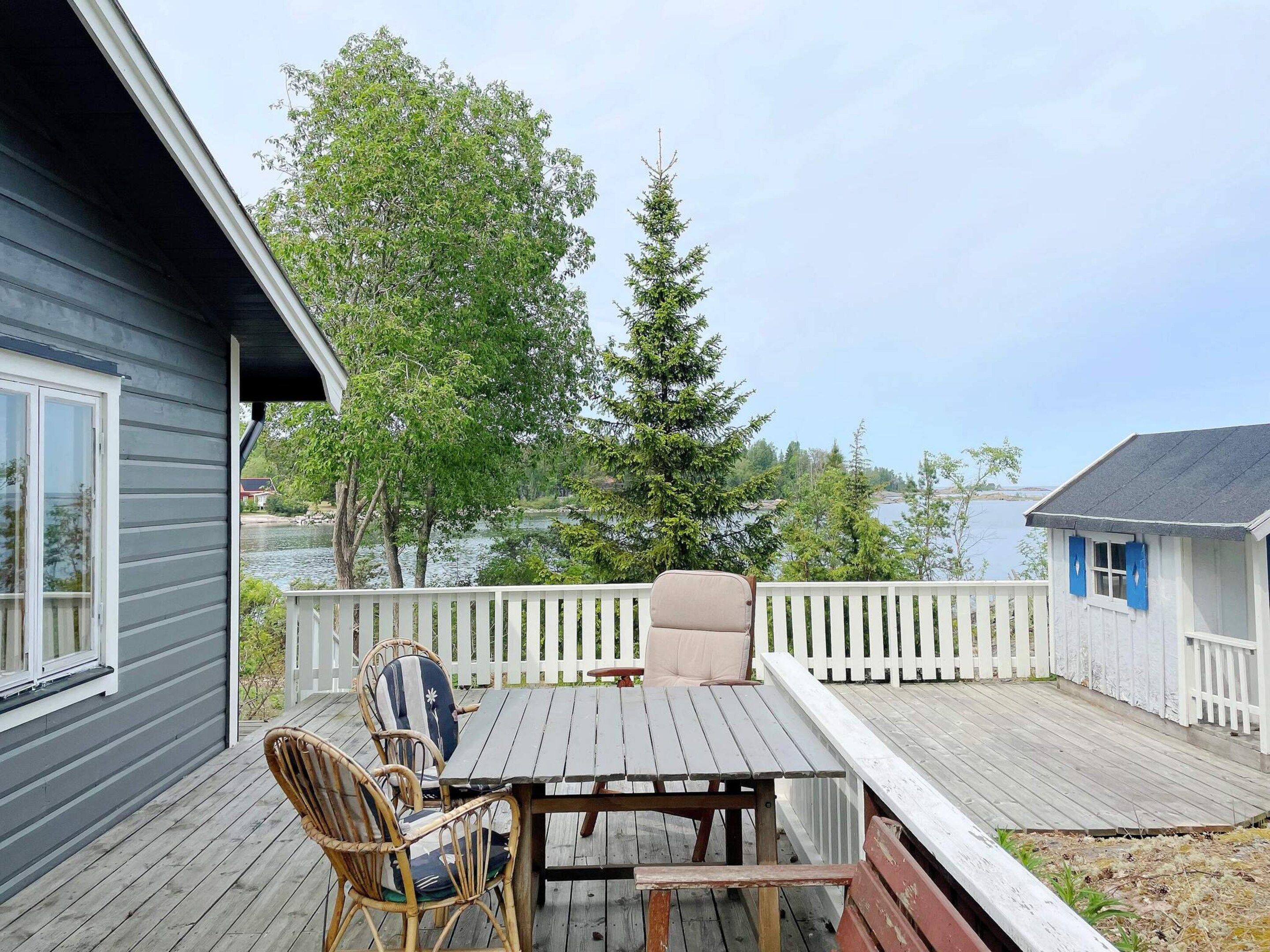 A deck with a table and chairs, a white picket fence, and a view of a lake and trees.