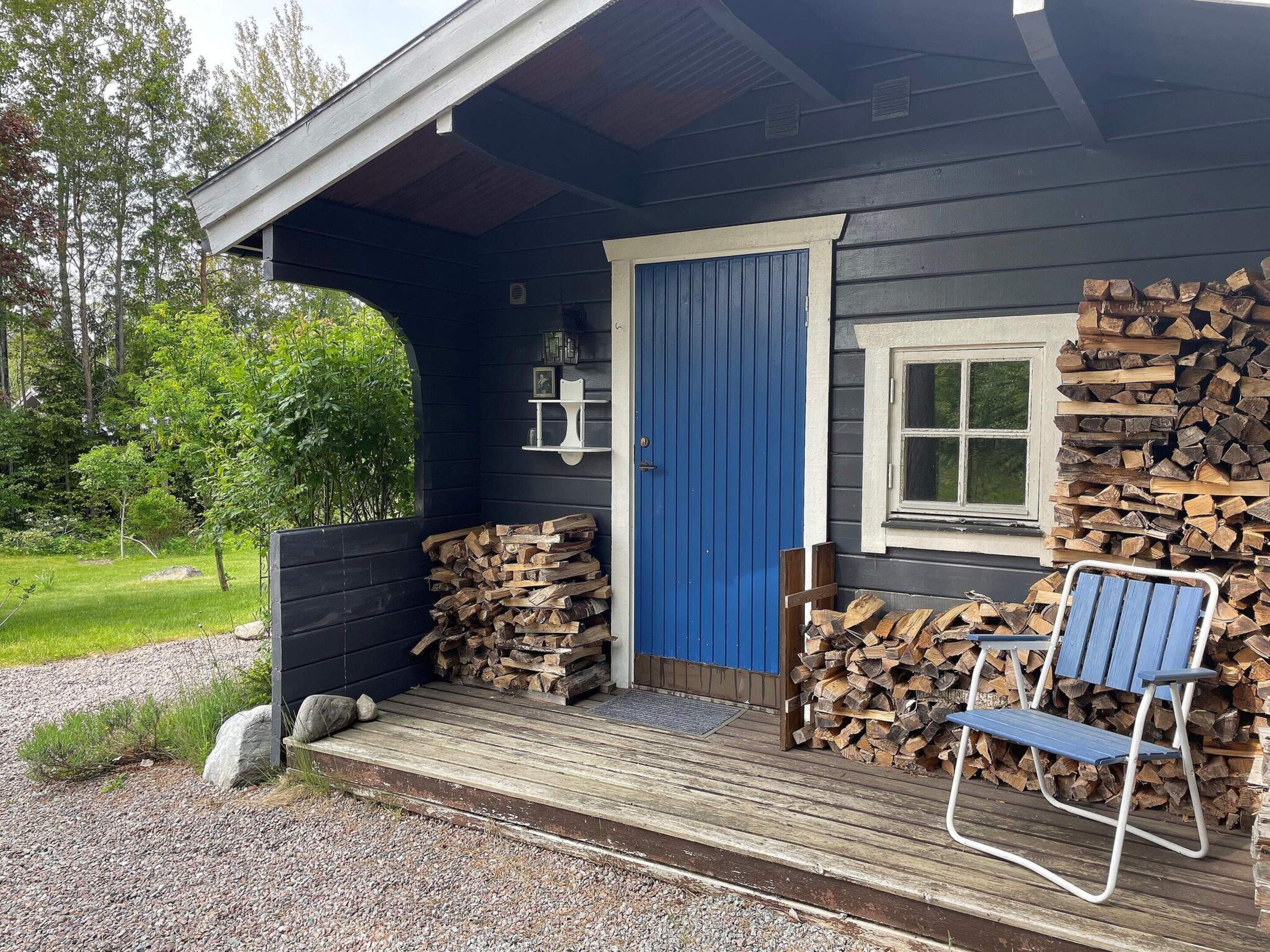 A cabin with a blue door, a wooden deck, and a chair outside.