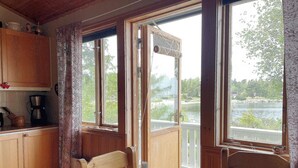 A cozy kitchen with wooden cabinets, a coffee maker, and a table with a candle. Large windows offer a view of a lake and greenery. - 4 Star Holiday Home in Vaddo (Väddö)
