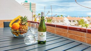 A table with a bottle of VinaSol wine, a bowl of fruit, and two glasses on a balcony overlooking a residential area. - Garden city with ocean view&heated pool (Costa Adeje)