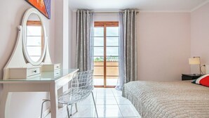 A hotel room with a bed, a desk with a mirror, a chair, a window with curtains, and a view of the outdoors. - Garden city with ocean view&heated pool (Costa Adeje)