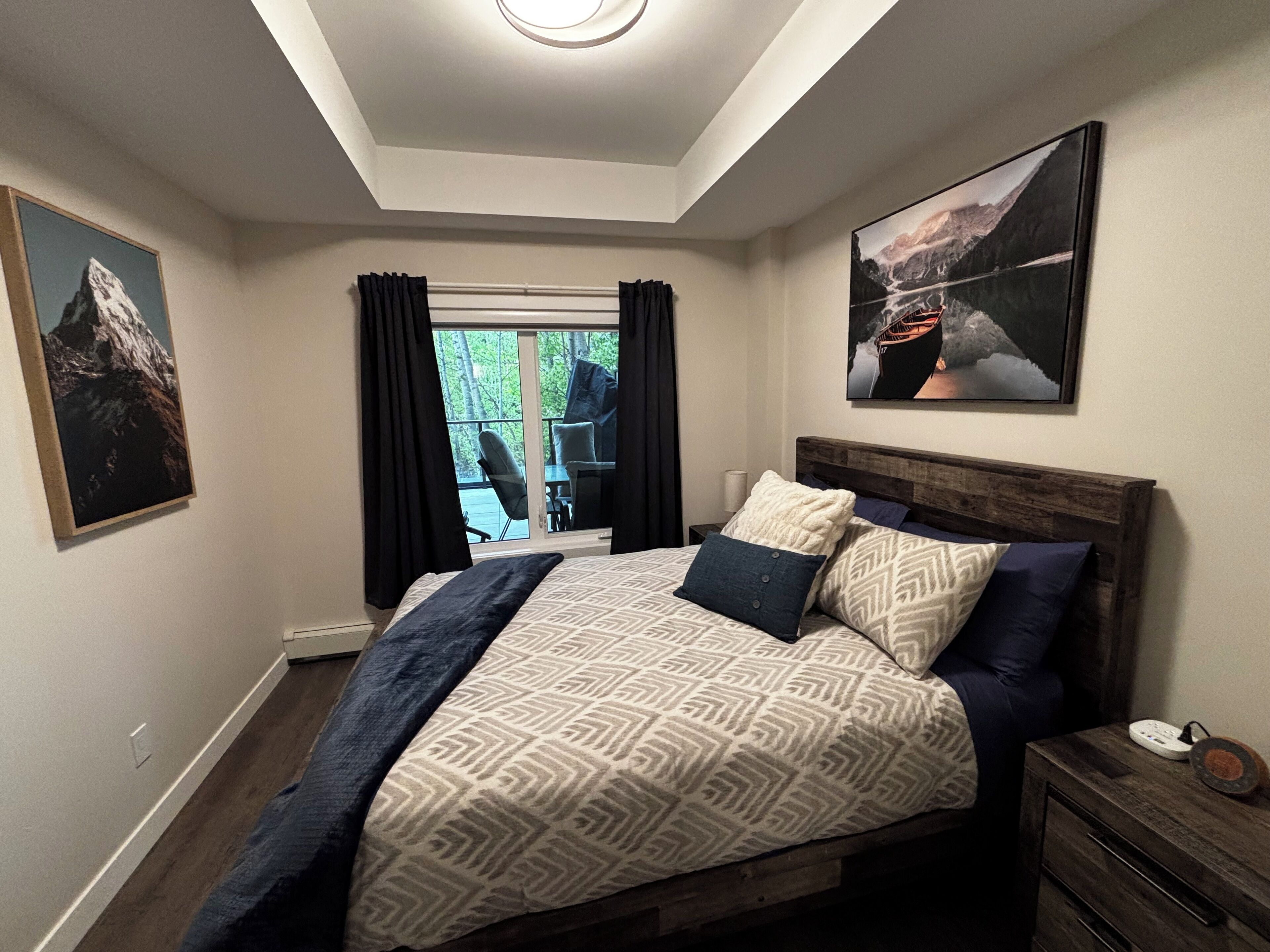 Une chambre à coucher comprenant un lit, une table de chevet, une fenêtre avec des rideaux et deux tableaux accrochés au mur.