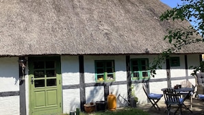 Ein traditionelles Haus mit einem strohgedeckten Dach, einer grünen Tür, weißen Wänden und grünen Fensterrahmen.