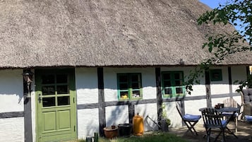 Una casa tradicional con techo de paja, puerta verde, paredes blancas y marcos de ventana verdes.
