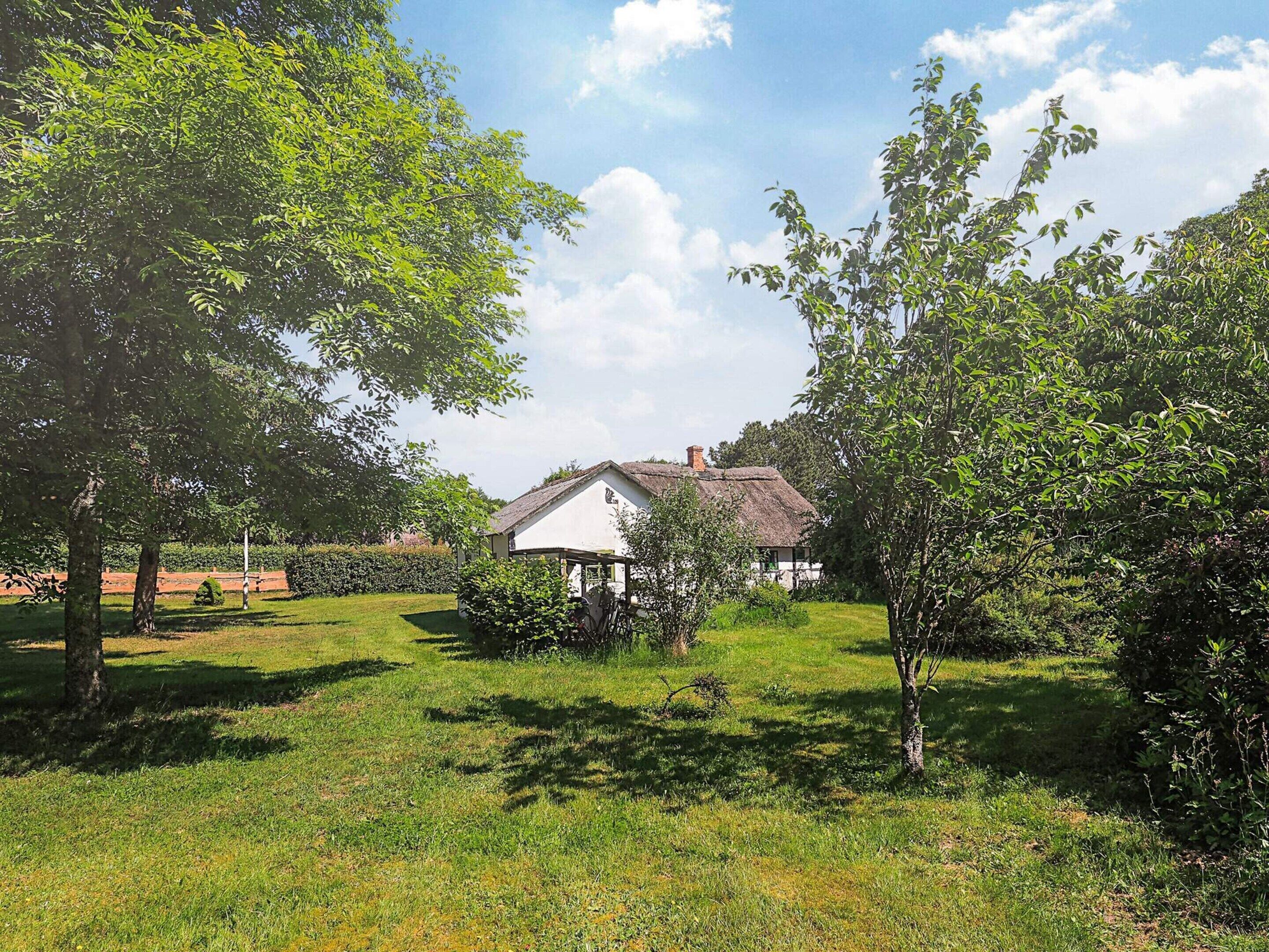 Een huis met rieten dak, omgeven door een verzorgd gazon en bomen.
