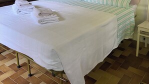 Una cama bien hecha con ropa de cama a rayas, una pila de toallas dobladas, una mesita de noche pequeña y un televisor sobre un mueble.