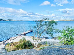 A rocky shoreline with a pier extending into a calm body of water, surrounded by sparse vegetation and distant hills. - 4 Star Holiday Home in Myggenas (Myggenäs)