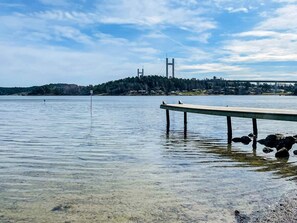 A calm body of water with a wooden dock extending into it, a distant bridge, and a forested hill in the background. - 4 Star Holiday Home in Myggenas (Myggenäs)