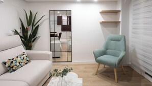 A modern living room with a white sofa, a teal armchair, a marble coffee table, and a large potted plant.