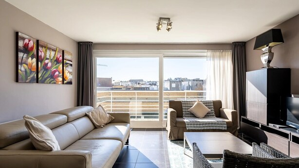 Una sala moderna con un sofá, una mesa de centro y un televisor. Hay un balcón con vistas a la ciudad.