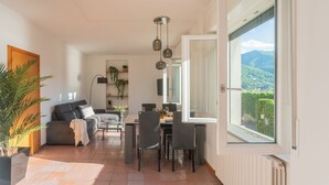 Ein großzügiger Wohnbereich mit Esstisch, Stühlen, einer Couch und einem großen Fenster mit Blick auf die Berge.