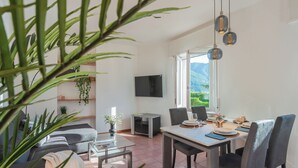 Ein modernes Wohnzimmer mit Essbereich, einem Flachbildfernseher und einem großen Fenster mit Blick ins Freie.