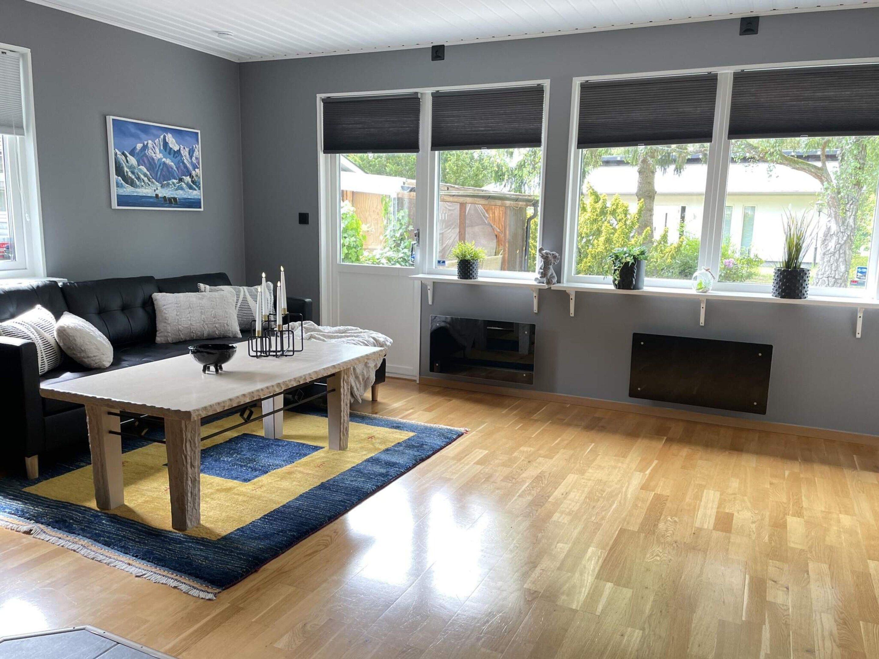 A living room with a black leather sofa, a wooden coffee table, a fireplace, and large windows with blinds.