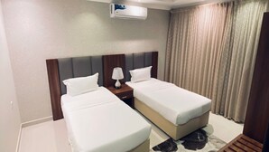 Ein Hotelzimmer mit zwei Betten, einer Decken-Klimaanlage, einem Nachttisch mit Lampe und einem gemusterten Teppich.